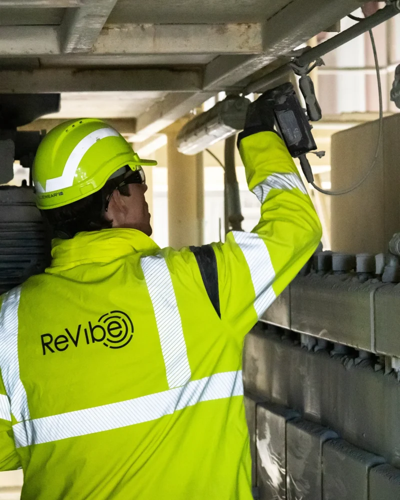 revibe-in-aggregate-plant-equipment A person in ReVibe jacket and helmet inspecting vibration monitoring equipment.